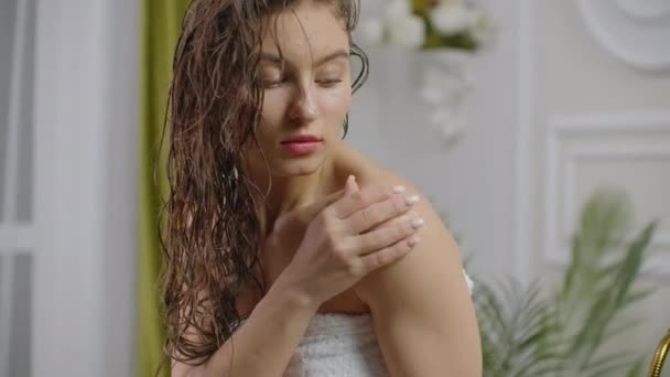 Женщина наносит крем на кожу в ванной комнате, сидя на ванне . — стоковое видео