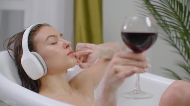 Mujer bastante joven escuchando música en los auriculares mientras toma el baño. Chica atractiva relajante tiene descanso en casa. Cuarto de baño ecológico interior. Aliviar el estrés y sentirse bien. Buen disfrute de contenido — Vídeo de stock