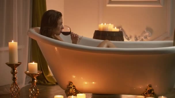 Mulher tomando banho com prazer, deitada na banheira com espuma e bebendo vinho tinto, passando um tempo em resort de spa de luxo . — Vídeo de Stock