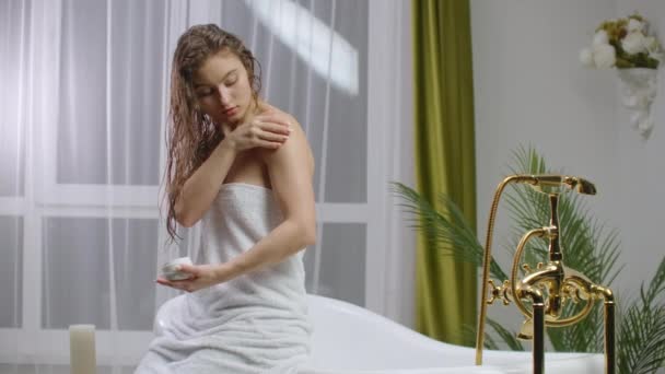 Belleza y cuidado corporal dolor de codo femenino y concepto de cuidado de la salud. cámara lenta de mujer caucásica aplicación crema crema hidratante relajante en la cama en blanco acogedor apartamento cerca de la ventana . — Vídeo de stock