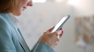 Yakın plan: Bir terzilik stüdyosunda cep telefonuyla müşterilere mesaj yazan genç bir kadın tasarımcı iş kadını.