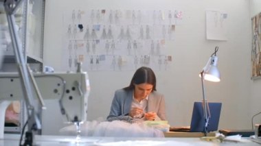 Atölyedeki kız, elinde boncuk ve mücevher ile masada oturuyor. Elbiseler dikin ve gece elbiselerini kristallerle süsleyin.