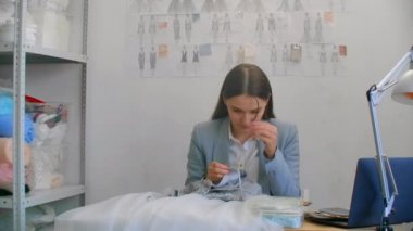 Stüdyo elbisesi giyen genç bir tasarımcı kız. Elbise dikmek boncuk ve mücevher dikmek. Terzi stüdyoda bir elbise dekore ediyor.