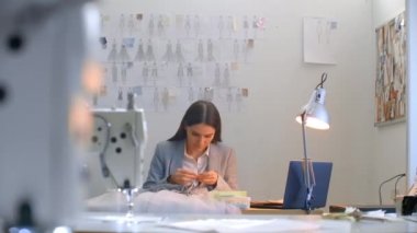 Stüdyo elbisesi giyen genç bir tasarımcı kız. Elbise dikmek boncuk ve mücevher dikmek. Terzi stüdyoda bir elbise dekore ediyor.