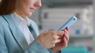 Yakın plan: Takım elbiseli genç bir kadın terzilik stüdyosunda cep telefonuyla bir dikiş atölyesinde müşterilere mesaj yazıyor. Ofiste bir mesaj yazıyorum.