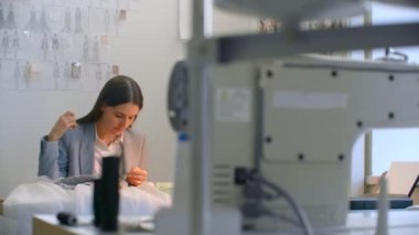 Atölyedeki kız, elinde boncuk ve mücevher ile masada oturuyor. Elbiseler dikin ve gece elbiselerini kristallerle süsleyin.