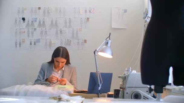 Eine junge Designerin macht ein Kleid im Studiokleid. Schneiderei Atelier näht Perlen und Schmuck. Näherin schmückt Kleid im Atelier — Stockvideo