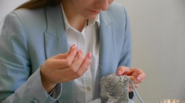 Atölyedeki kız, elinde boncuk ve mücevher ile masada oturuyor. Elbiseler dikin ve gece elbiselerini kristallerle süsleyin.