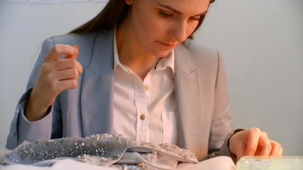 Eine junge Designerin näht ein Kleid im Studiokleid. Herstellung von Kleidern, Perlen und Schmuck. Näherin schmückt Kleid im Atelier — Stockvideo