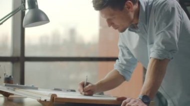 Erkek bir mimar kağıda bir bina çizer. Evlerin ve mobilyaların tasarımını incelemek için. Karatahtaya modern ofis çizimi