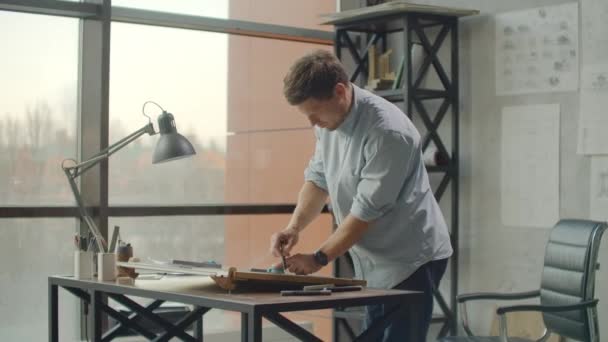 A man is a young modern architect sitting at a table drawing a plan of the building and developing a design, sitting in an office in the Sitel loft near a large window. — Stock videók