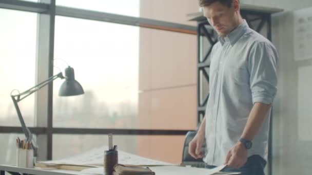 Hipster-Ingenieur arbeitet mit Blaupausen. Schießen Sie von oben. Junger Bauingenieur im Büro. Bärtiger Mann macht Skizzen. Loftstil, minimalistisches Interieur, Zeichnungen auf dem Tisch. — Stockvideo