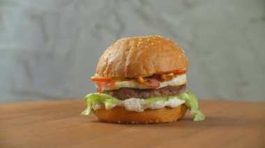 Hamburger tahta bir tahtanın üzerinde döner. Salata peynirli ve domatesli bir hamburger gri bir duvara yaslanır..