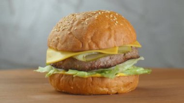 Hamburger tahta bir tahtanın üzerinde döner. Salata peynirli ve domatesli bir hamburger gri bir duvara yaslanır..