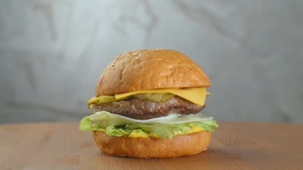 Gran hamburguesa con chuleta de res, tomates, champiñones y pepinos con queso derretido gira sobre un tablero de madera sobre fondo claro — Vídeo de stock