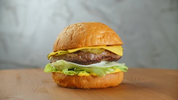 Große Burger mit Rinderschnitzel, Tomaten, Pilzen und Gurken mit geschmolzenem Käse dreht sich auf einem Holzbrett auf hellem Hintergrund — Stockvideo
