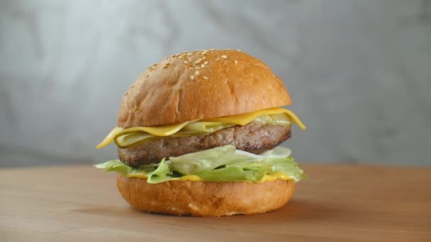 Mňam pojetí fast foodu. Čerstvý domácí grilovaný burger s masovou plackou, rajčaty, okurkou, salátem, cibulí a sezamovými semínky. Nezdravý životní styl. Pozadí potravin — Stock video
