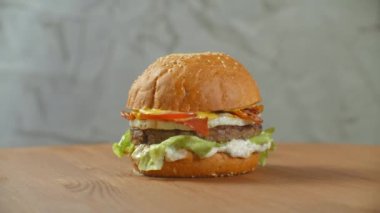 Açık renkli ahşap bir gemide üzerinde büyük hamburger biftek pirzola, domates, mantar ve salatalık eritilmiş peynir ile döner