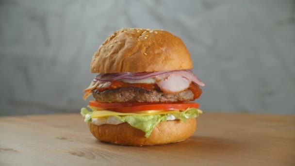 Pyszna koncepcja fast foodów. Świeży domowej roboty grillowany burger z patty mięsa, pomidory, ogórek, sałata, cebula i nasiona sezamu. Niezdrowy styl życia. Kontekst żywności — Wideo stockowe