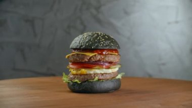 Kara burger. Yeşil sebzeli. İki pirzolalı bir hamburger ahşap bir tahtanın üzerinde döner. Koca şişko Burger.