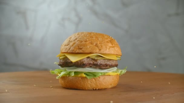 Ve zpomaleném filmu, sezamová semínka padají na točící se hamburger. Hamburger na dřevěné desce. — Stock video