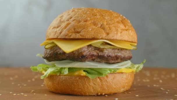 Ve zpomaleném filmu, sezamová semínka padají na točící se hamburger. Hamburger na dřevěné desce. — Stock video