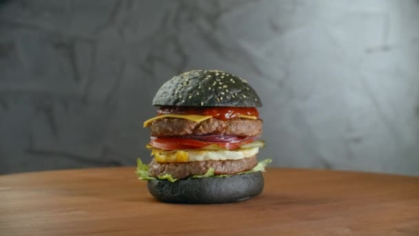 Hamburguesa negra. Con verduras griegas. Una hamburguesa con dos chuletas gira sobre una mesa de madera. Hamburguesa gorda grande — Vídeos de Stock