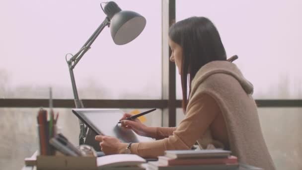 A young designer girl draws on a modern graphic screen using a workstation in an office with large Windows. Create logo design and graphics. — ストック動画