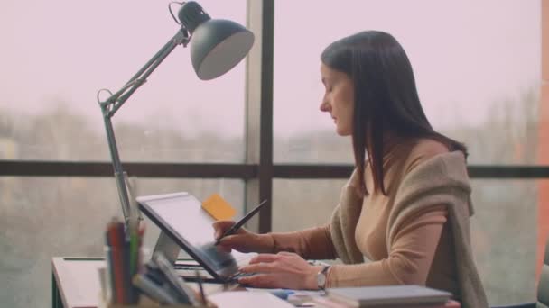 Ein professioneller Designer im Büro zeichnet mit einem Stift auf einem Grafiktablett in einem Büro mit riesigen Fenstern im Loftstil. modernes Büro des Grafikdesigners und Schöpfers — Stockvideo