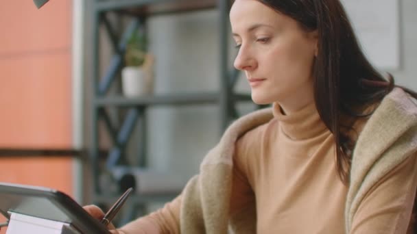Mladá žena sedí za stolem a kreslí, píše a používá pero s digitálním počítačem. Ruce s perem. — Stock video
