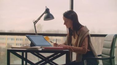 Bir kadın grafik tasarımcı, geniş pencereli ve boyalı bir ofiste bir stil ve bilgisayar ekranı kullanarak çalışır. Tasarımcılar için dokunmatik ekranlı çalışma istasyonu. 