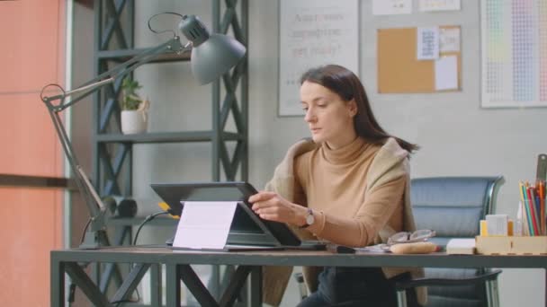 Eine Grafikerin arbeitet in einem Büro mit großen Fenstern und malt mit einem Stift und einem Computer-Touchscreen. Arbeitsplatz mit Touchscreen für Designer. — Stockvideo