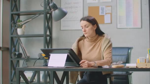 Молода жінка сидить на її столовій полиці малює, пише і використовує ручку з цифровим планшетним комп'ютером. Руки з ручкою . — стокове відео