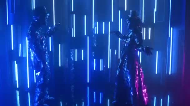 반짝이는 의상을 입고 네온 벽을 등지고 춤을 추는 두 로봇 댄서가 서로 더 가까와 지고 있다 — 비디오