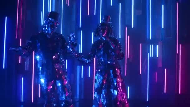 Lustige und fröhliche Tänzer in funkelnden Kostümen, die das Licht synchron auf dem Hintergrund einer Neonwand reflektieren — Stockvideo