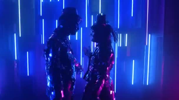 Двоє танцюристів-роботів у блискучих костюмах танцюють на неонових стінах — стокове відео