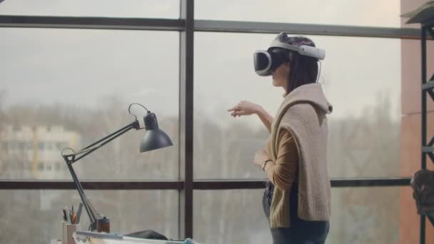 Женщина-инженер в шлеме виртуальной реальности возле большого окна своими руками имитирует работу интерфейса. Проектирование будущего, концепция виртуальной архитектуры и дизайна, приложения — стоковое видео
