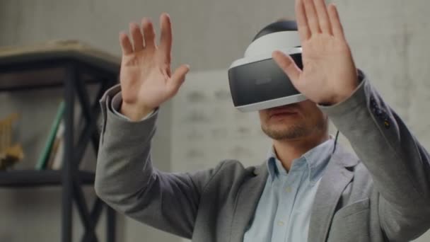 Moderne man ingenieur-ontwerper in het kantoor met grote ramen staat in een virtual reality helm maakt gebruik van gebaren om het project te beheren zonder het kantoor te verlaten. Bouwcontrole. Ontwerp project — Stockvideo