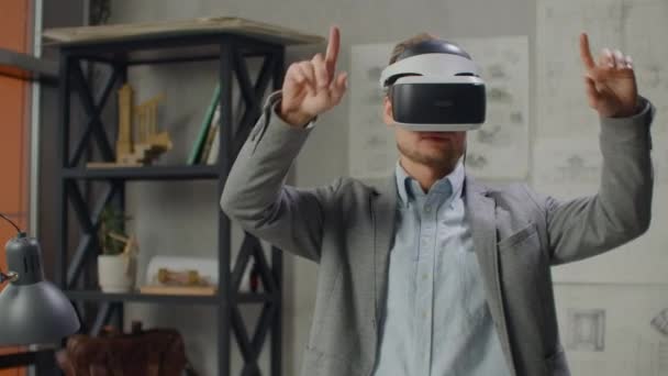 Joven diseñador en oficina en casco de realidad virtual con las manos hace movimientos imitando el trabajo de interfaz gráfica — Vídeos de Stock