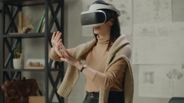 Молода жінка-архітектор в офісі в шоломі віртуальної реальності з руками виконує рухи, що імітують роботу графічного інтерфейсу — стокове відео