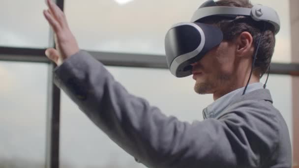 Man di helm realitas maya terhadap latar belakang jendela besar di kantor di tempat kerja. Insinyur desain bekerja di virtual reality helm — Stok Video