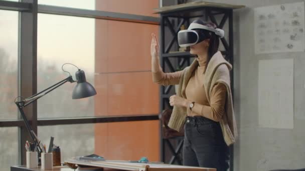 Nowoczesna kobieta inżynier-projektant w biurze z dużymi oknami stoi w kasku wirtualnej rzeczywistości używa gestów do zarządzania projektem bez wychodzenia z biura. Kontrola budowy. Projekt projektowy — Wideo stockowe