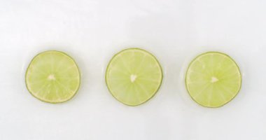 Su yavaş çekimde sıçrar. Üst manzara: beyaz arka planda suyla yıkanmış üç dilim yeşil limon..