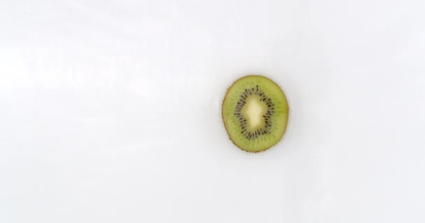 Slow motion water splash on one slice of kiwi lying on a white background in water. — Stock Video