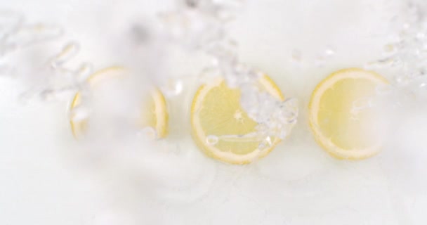 Pomalý pohyb vody stříkající na tři plátky citronu ležící na bílém pozadí ve vodě. — Stock video