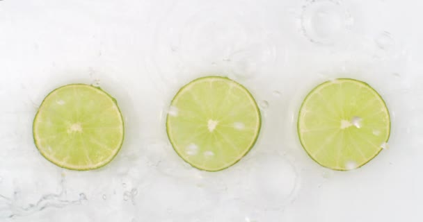 Slow motion water splash on three slices of green lime lying on a white background in the water. — Stock Video