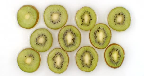 Water splashes in slow motion. Top view: several circles of kiwi is washed with water on a white background. chopped fruit — 비디오