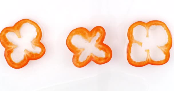 Slow motion water splash on three slices of pepper lying on a white background in water. — Stock Video