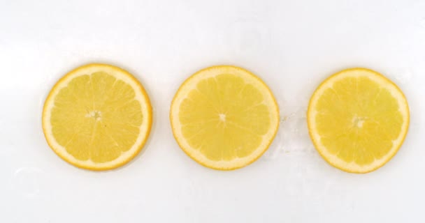 Slow motion water plons op drie plakjes sinaasappel liggend op een witte achtergrond in water. — Stockvideo