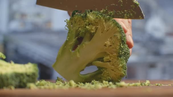 Snijd met een mes op een houten plank van dichtbij broccoli in de keuken. versnippering. — Stockvideo